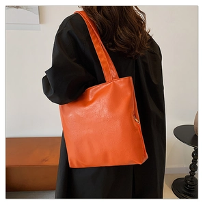 Detail of a vibrant orange faux leather tote bag with soft texture and metallic zipper side