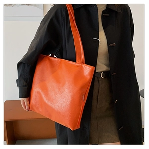 Detail of orange tote bag showing pebbled leather texture and hidden side zipper on model