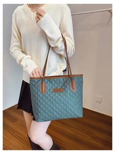 Detail of dark green quilted tote bag featuring brown leather handles and brand tag