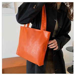 Detail of a bright orange tote bag with high-shine wrinkled texture and side zipper