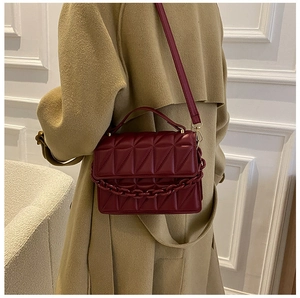 Detail of burgundy quilted crossbody bag with metal chain strap and top handle design