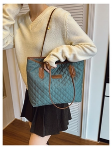 Detail of dark green quilted tote bag with brown leather handles and fashion logo patch