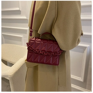 Close-up of dark red quilted PU leather handbag with decorative thick chain and texture