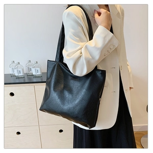 Detail of minimalist black large tote bag showing natural leather texture and shoulder strap