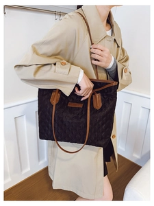 Detail of black quilted tote bag with brown straps and brand plaque worn on shoulder