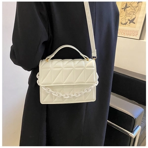 Detail of cream quilted bag with acrylic chain link and top handle worn by a model
