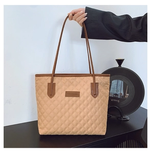 Close-up of the quilted diamond pattern and leather logo on the beige tote bag