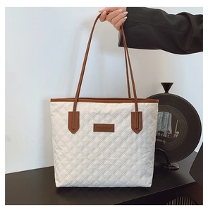 Close-up of white quilted tote bag featuring brown leather logo patch and contrast trim