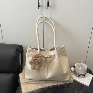 Elegant beige leather tote bag with buckle detail and plush bear charm on a cozy background