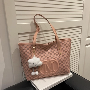 Pink tote bag with M-pattern print and cloud charm displayed on a vintage book