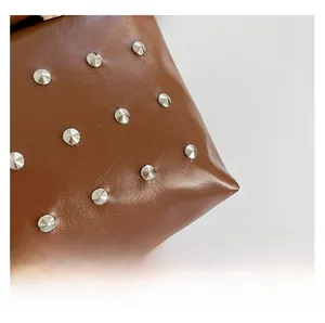 Detail view of premium brown leather texture with silver metal rivet studs on the handbag