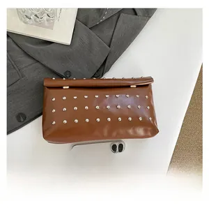 Brown leather clutch with silver studs shown next to a smartphone for size reference