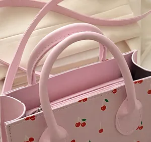 Detail van de handvaten, metalen rits en kersenprint op de roze handtas voor dames