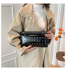 Close-up of black glossy envelope bag with silver studs held by a model in a trench coat