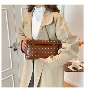 Brown envelope clutch bag with silver rivets held by a model wearing a beige trench coat