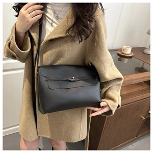 Detail of a minimalist black leather crossbody bag styled with a wool coat in warm lighting