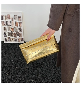 Detail of golden metallic envelope clutch with silver rivets held by a model for fashion party