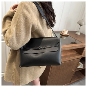 Close-up of minimalist black leather shoulder bag with retro metal buckle on a khaki coat