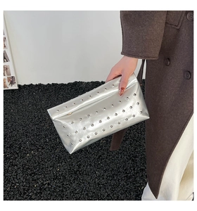 Detail of silver metallic rivet clutch bag held by a model on a modern stone background