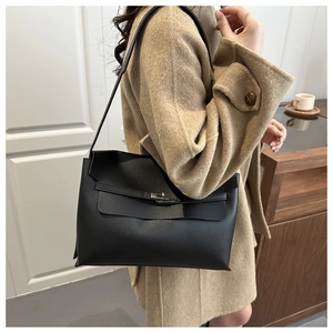 Detail of minimalist black pebbled leather shoulder bag with silver buckle on a wool coat