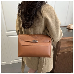 Detail view of a brown leather shoulder bag with silver turn-lock and decorative strap