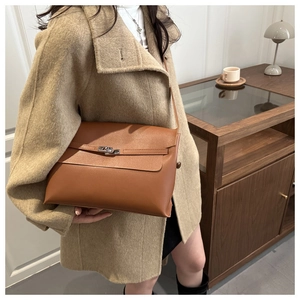 Close-up of brown leather underarm bag with silver metal lock on a beige coat