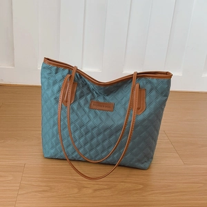 Blue quilted tote bag with brown leather handles and fashion logo on light wood floor