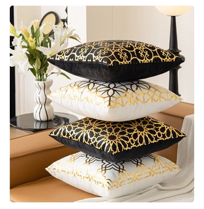 Detail of four black and white pillow covers with gold foil geometric patterns on a sofa