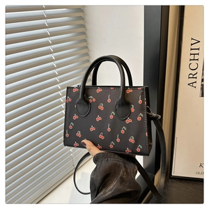 Detail van zwarte handtas met kersenprint, rond handvat en afneembare schouderriem