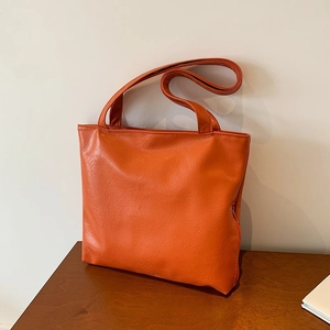 Minimalist orange PU leather tote bag with metal zipper on a wooden table, 2024 fashion