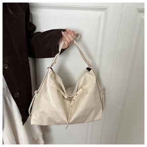 Detail of a large beige soft leather tote bag with thin straps and gold metal buckles