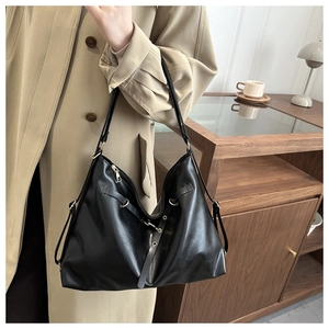 Lifestyle shot of a black leather tote bag with metallic buckle worn with a beige trench coat