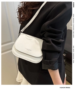 Close-up of a white leather flap crossbody bag with embossed lettering on a model