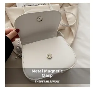 Detail view of the metal magnetic snap closure on the white faux leather saddle bag
