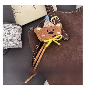 Detail of a brown plush bear charm with a yellow bow attached to a faux suede tote bag