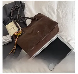 Detail of vintage brown matte tote bag with teddy bear charm on a white bedsheet