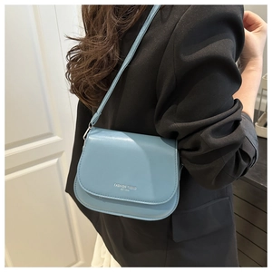 Detail of light blue crossbody bag with silver lettering on black blazer model outfit