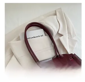 Macro detail of wine red glossy patent leather tote bag on a cream blazer