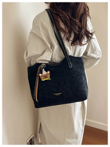 Model wearing large black matte tote bag with cute bear charm and tassel detail