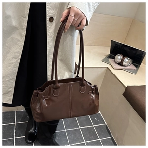 Detail of a brown glossy leather shoulder bag with fine stitching on a wooden bench
