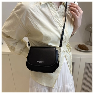 Detail of a black matte leather saddle bag worn by a model in a minimalist home setting