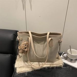 Minimalist beige tote bag with cute plush bear charm on a warm textured background