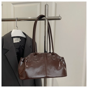 Detail of glossy brown patent leather shoulder bag with sleek metal buckles and strap
