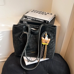 Vintage black faux leather tote bag with white stitching and bear charm on a seat