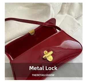 Detailed close-up of the elegant golden metal twist-lock on a dark red patent leather bag