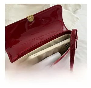 Interior storage of the burgundy patent leather underarm bag showing phone and cosmetics