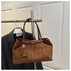 Detail of brown faux suede tote bag featuring a decorative belt buckle and leather tag