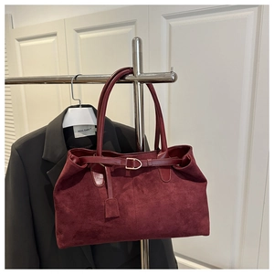 Detail of burgundy suede tote bag with metal buckle and leather straps hanging on a rack