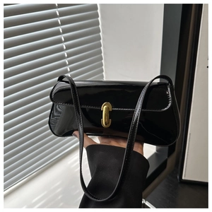Detail of glossy black patent leather baguette bag featuring a gold metal lock closure