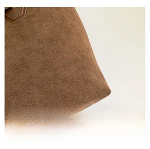 Gros plan d'un sac cabas en daim marron montrant la texture du cuir mat et les détails des fibres